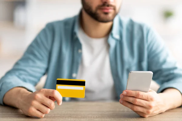 Ψώνια στο σπίτι. Κοντινό πλάνο του νεαρού που κατέχει πιστωτική κάρτα και smartphone, κάνοντας online αγορά στο τραπέζι σε εσωτερικούς χώρους — Φωτογραφία Αρχείου