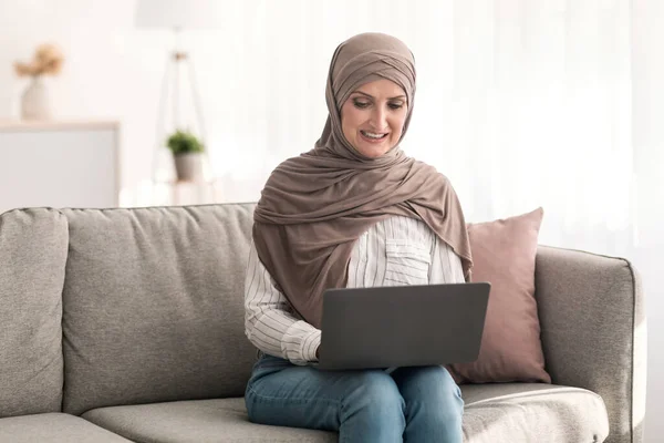 Зрелая женщина с Ближнего Востока с помощью ноутбука просмотра Интернета сидя дома — стоковое фото