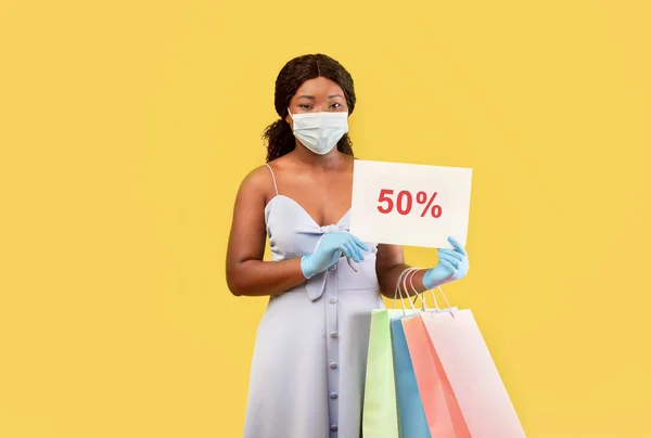 Černá dáma v lékařské masce a gumových rukavicích držící nákupní tašky a nápis FIFTY PERCENT OFF, nabízející obrovský prodej — Stock fotografie