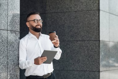 Olgun iş adamı dijital tablet kullanıyor ve kahve içiyor. Açık havada dinlenirken, boşluğu kopyalıyor.