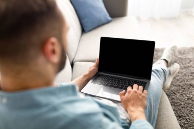 Evdeki rahat koltukta dizüstü bilgisayar kullanan tanınmayan genç adam, ekranda web sitesi tasarımı için model