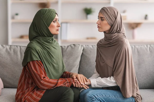 Infelice maturo musulmano madre e adulto figlia holding mani indoor — Foto Stock