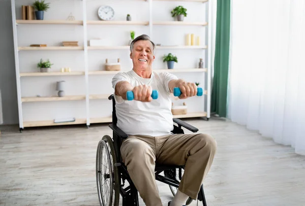 Vidám mozgássérült férfi tolószékben rehabilitációt végez súlyzókkal az idősek otthonában. — Stock Fotó