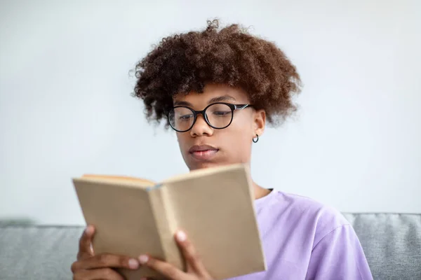 Skupiona Afroamerykańska nastolatka czytająca książkę, ciesząca się urzekającą historią w domu — Zdjęcie stockowe