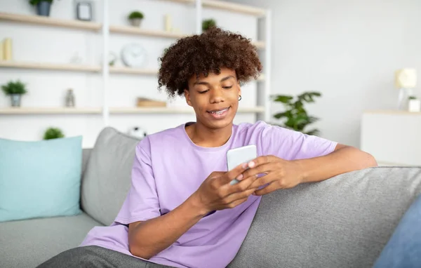 Cool černošky teenager s mobilním telefonem studuje online, chatování s přítelem, vysílání v sociálních sítích z domova — Stock fotografie