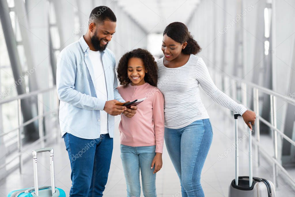 Happy black family traveling, holding documents in airport