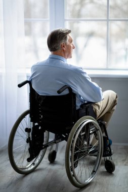 Uzun boylu, tekerlekli sandalyedeki yaşlı adam depresyonda, huzurevinde yalnızlık çekiyor.