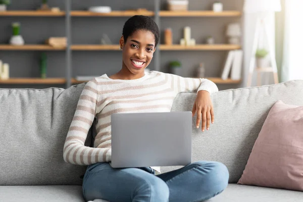 Retrato de senhora africana sorridente sentada no sofá com laptop em voltas — Fotografia de Stock