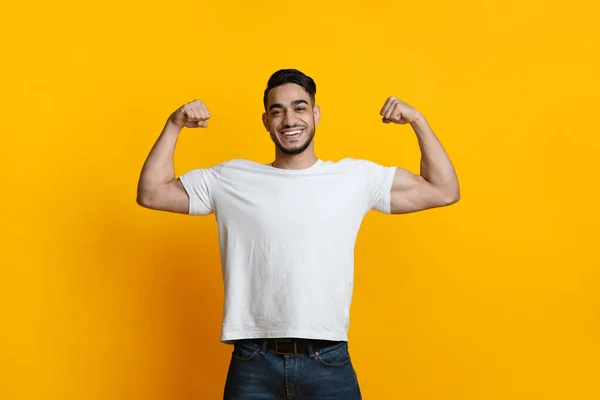 Sonriente árabe mostrando sus bíceps en amarillo — Foto de Stock