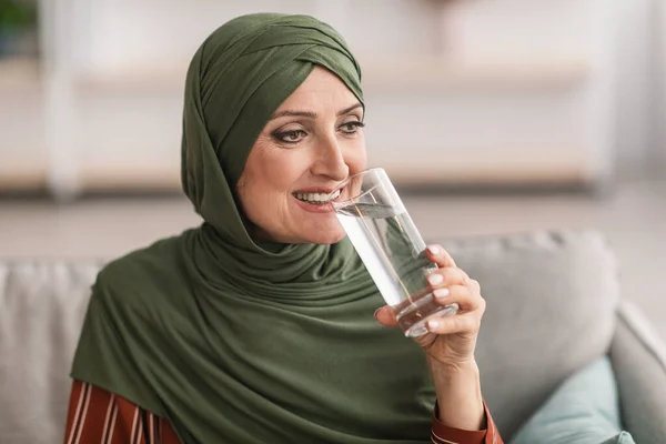 Wanita muslim senior yang ceria di Hijab minum air di rumah — Stok Foto