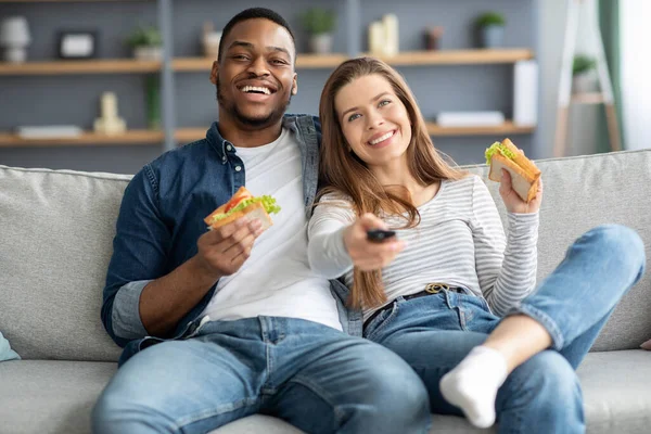 Casais Lazer. alegres jovens amantes inter-raciais assistindo TV e comer sanduíches — Fotografia de Stock