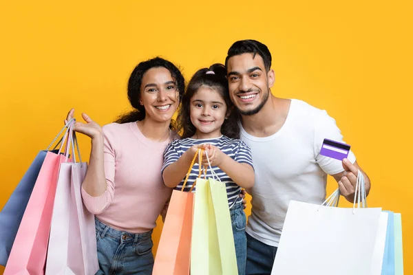 Pais árabes alegres e pequena filha segurando sacos de compras e cartão de crédito — Fotografia de Stock