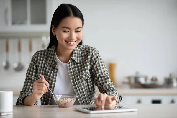 若いアジアの女性は朝食を持っており、デジタルタブレットを使用して — ストック写真
