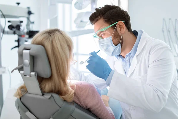 Homem dentista em máscara facial e óculos fazendo tratamento — Fotografia de Stock