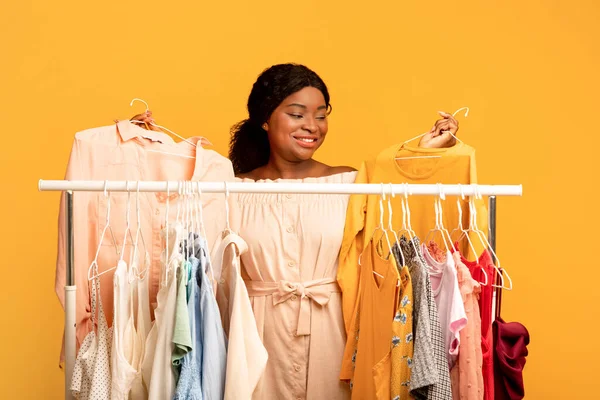 Mulher negra em pé perto de rack de roupas cheio de roupas elegantes, escolhendo roupas de verão, compras para guarda-roupa sazonal — Fotografia de Stock