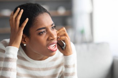 Hoş olmayan bir çağrı. Evde cep telefonuyla konuşan sinirli siyah bir kadının portresi.