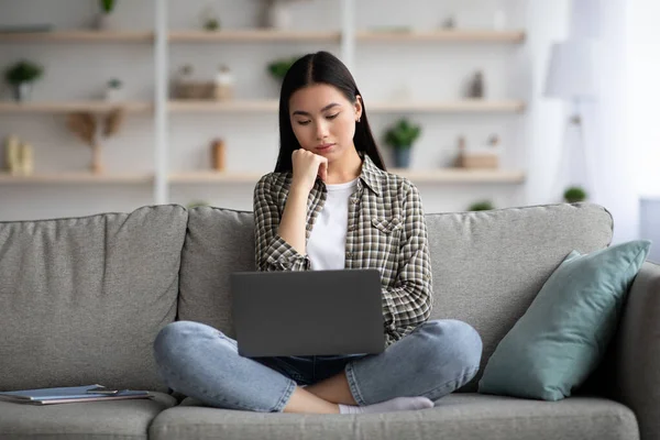 Pensativo asiático señora usando laptop, buscando trabajo en línea —  Fotos de Stock