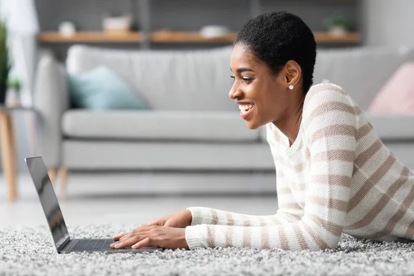 Vista lateral de alegre mujer negra usando ordenador portátil en casa —  Fotos de Stock