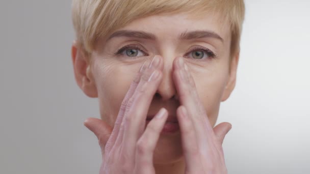 Belleza de mediana edad. Atractiva mujer madura haciendo masaje lifting facial, mirando a la cámara, fondo gris estudio — Vídeo de stock