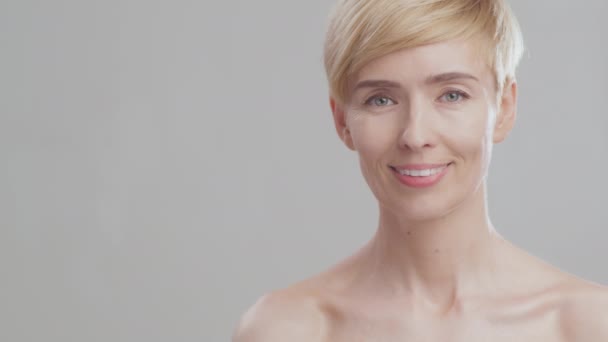 Positivo hermosa señora madura con hombros desnudos posando sobre fondo gris estudio con espacio vacío, sonriendo a la cámara — Vídeos de Stock