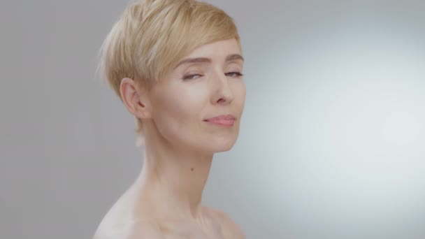 Potret profil wanita dewasa yang menarik menatap ke kamera dan tersenyum, berpose dengan bahu telanjang — Stok Video