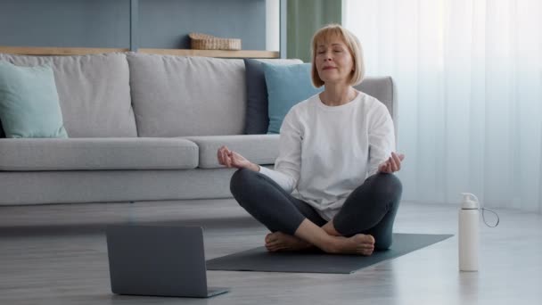 Seniorin meditiert am Laptop und sitzt in Lotus-Position — Stockvideo