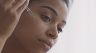 Cilt için vitamin. Genç Afrikalı Amerikalı kadın yüzüne serum uyguluyor, günlük güzellik prosedürlerini uyguluyor.