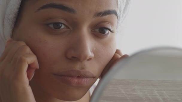 Самодельная подтяжка кожи. Молодая африканская американка делает массаж лица, смотрит на зеркало в ванной комнате после душа — стоковое видео