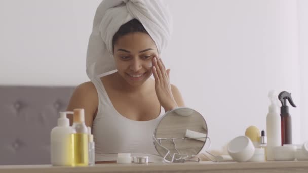 Spa-dag hemma. Ung afrikansk amerikansk dam tillämpa grädde på ansiktet hud efter dusch, njuta av skönhetsbehandlingar — Stockvideo