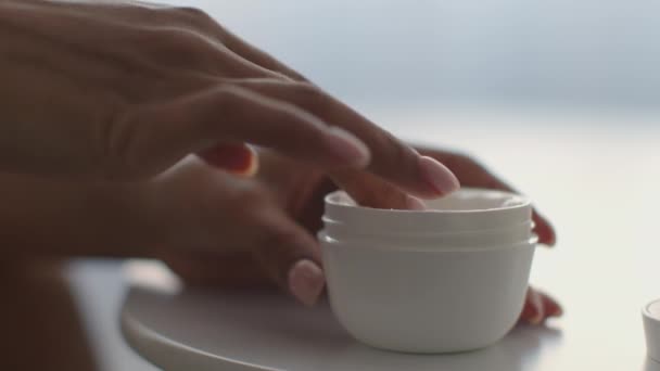 Cosmetici di bellezza a casa. Donna afroamericana irriconoscibile che prende la crema biologica dal barattolo e la applica sulle mani — Video Stock