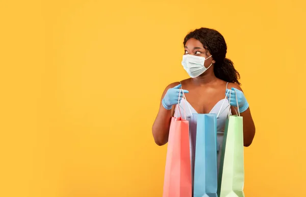 Compras seguras durante o covid. Mulher negra usando máscara facial e luvas de borracha, segurando sacos de papel, olhando para o espaço vazio — Fotografia de Stock