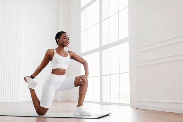 Joven mujer negra estirando la pierna haciendo ejercicio en la esterilla de yoga —  Fotos de Stock