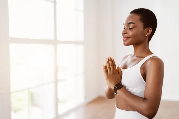 En svart kvinne som mediterer mens hun holder hender sammen i bønn. – stockfoto
