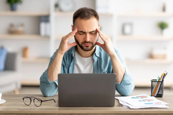 Giovane esausto stanco dopo aver lavorato sul computer portatile per troppo tempo, avendo mal di testa, massaggiando templi a casa — Foto Stock