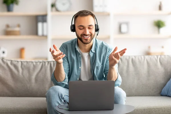 Szczęśliwy młody facet w słuchawkach podejmowania rozmowy wideo na laptopie w domu, rozmawiając z kamerą — Zdjęcie stockowe