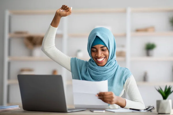 Business Success. Excited Black Islamic Lady In Hijab Reading Papers At Workplace