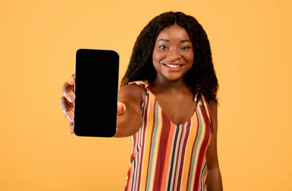 Fajna aplikacja na zakupy. Czarna kobieta pokazuje smartfon z pustym ekranem na pomarańczowym tle, makieta do projektowania — Zdjęcie stockowe