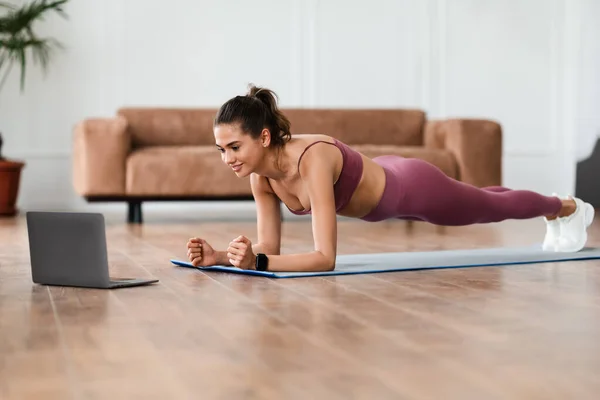 Jonge vrolijke vrouw doen plank op mat met pc — Stockfoto