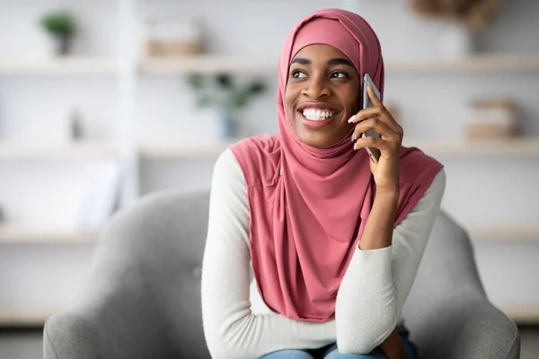 Vidám fekete muszlim nő Hidzsábon beszél mobiltelefonon otthon — Stock Fotó