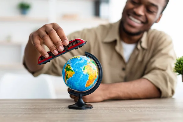 Homem negro brincando com trem modelo e globo em casa — Fotografia de Stock