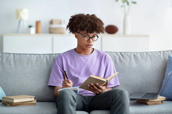Adolescente nero concentrato con libro di testo che prende appunti, studia a casa, si prepara per un esame importante — Foto Stock