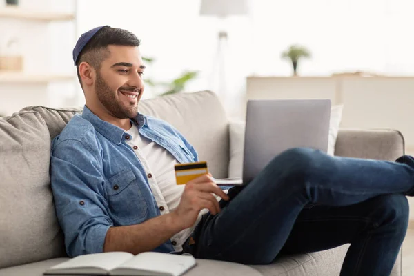 Χαμογελώντας εβραίος χρησιμοποιώντας φορητό υπολογιστή και πιστωτική κάρτα στο σπίτι — Φωτογραφία Αρχείου