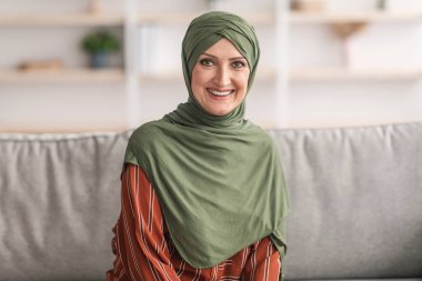 Evde tesettürlü, gülümseyen Müslüman bir kadının portresi