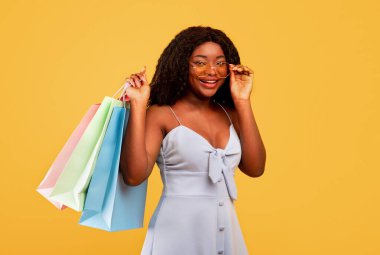Mevsimlik satışlar ve alışveriş. Parlak alışveriş torbaları taşıyan genç siyahi kadın, turuncu arka plan.