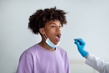 Klinikteki genç zenci hasta için oral koronavirüs PCR testi yapan doktor. Bulaşıcı hastalıkları önleme kavramı
