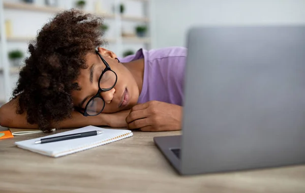 Cansado adolescente negro durmiendo en la mesa delante de la computadora portátil en casa, panorama —  Fotos de Stock