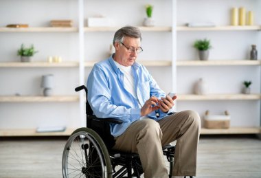 Tekerlekli sandalyedeki yaşlı adam akıllı telefon kullanıyor, mesajları kontrol ediyor, video izliyor, internette geziniyor.