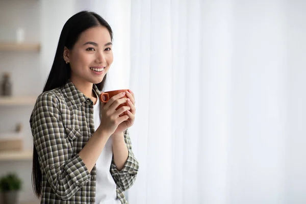 Dromerige aziatische dame genieten van 's morgens koffie in de woonkamer — Stockfoto