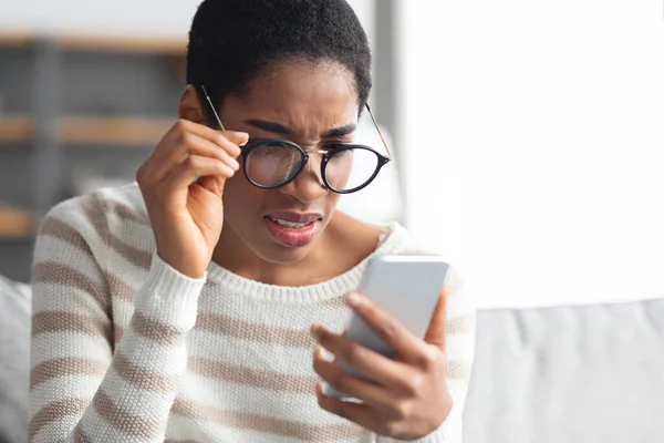 Má visão. Jovem mulher afro-americana em óculos olhando para a tela do smartphone — Fotografia de Stock