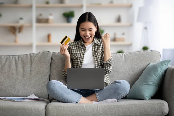 Емоційна жінка використовує ноутбук і кредитну картку вдома — стокове фото